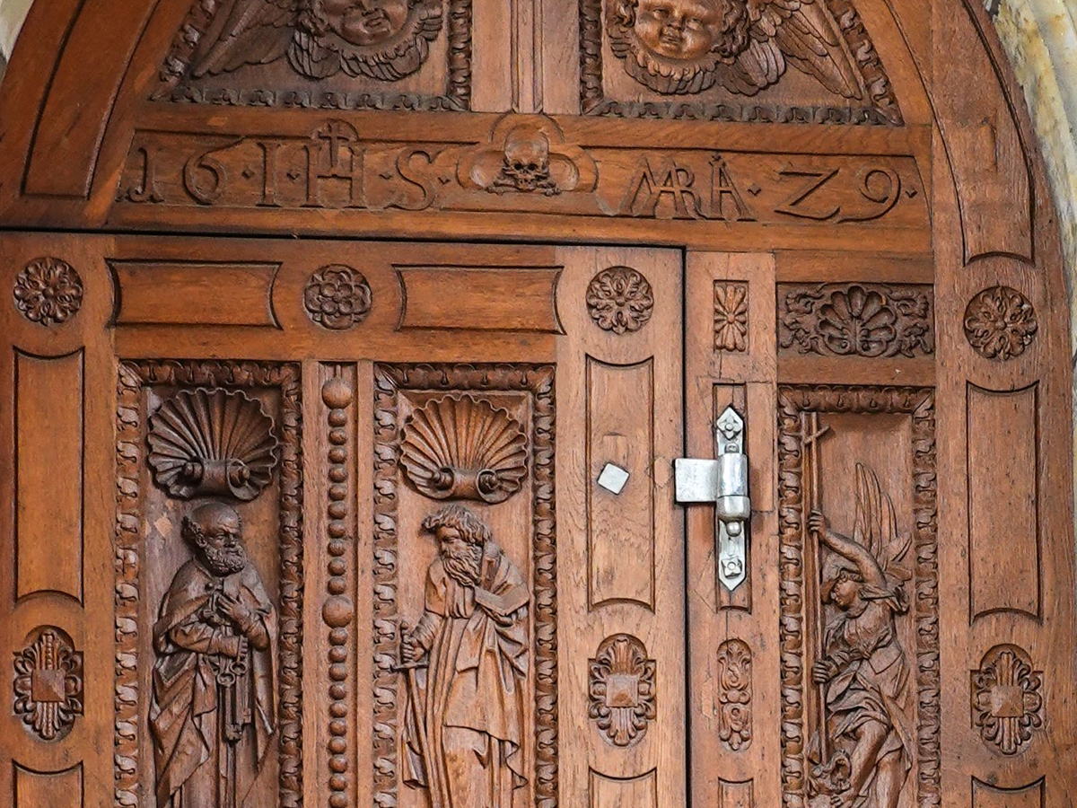 Detalle de puerta de madera tallada con relieves y herraje de forja